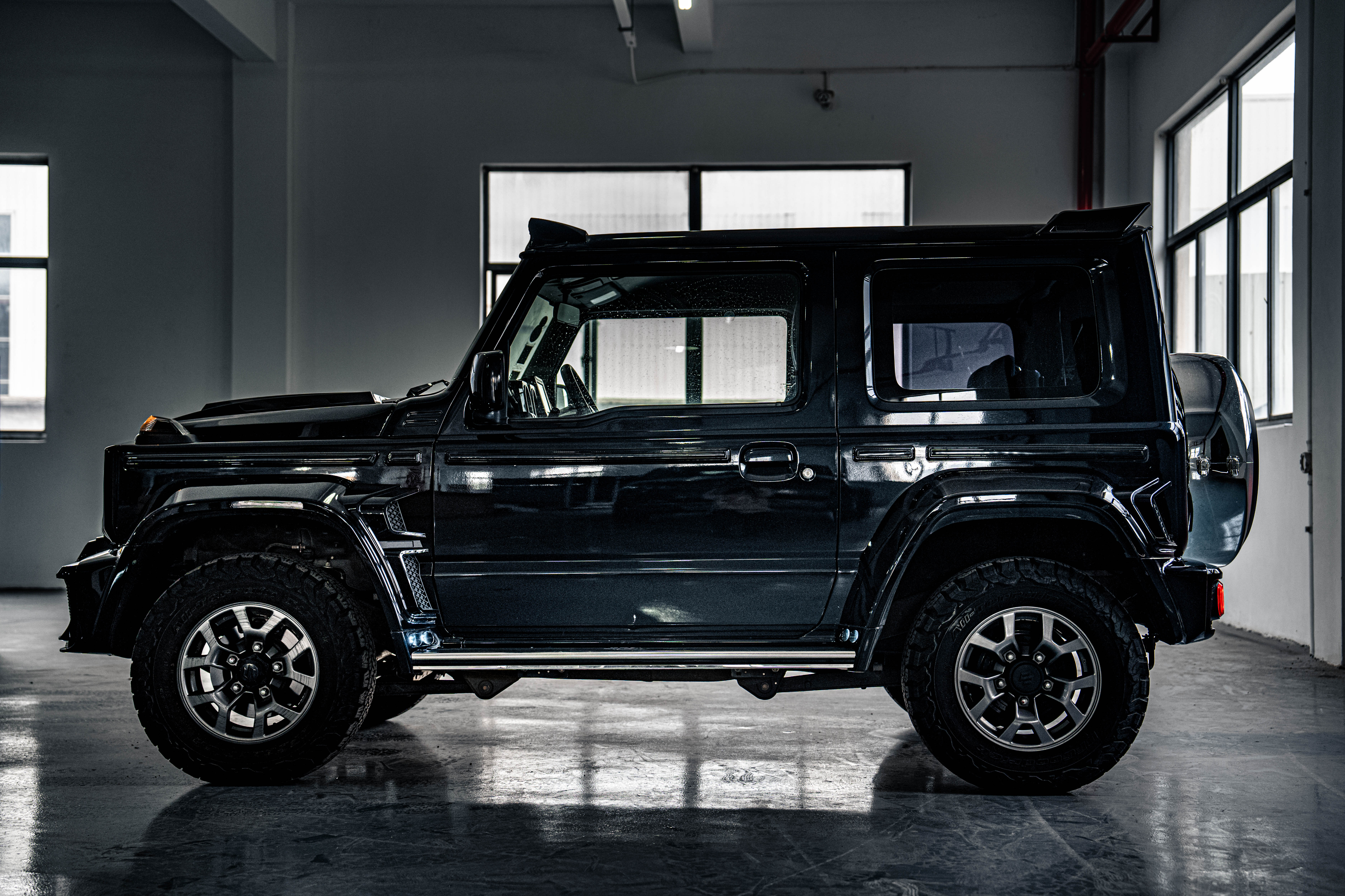 Black off-road SUV parked indoors with large tires and a spare tire mounted on the rear.